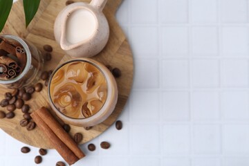 Tasty iced coffee in glass, milk and beans on white tiled table, flat lay. Space for text