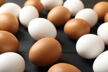 Many raw chicken eggs on black wooden table, closeup