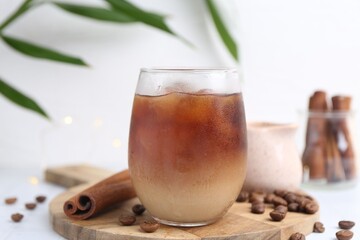 Tasty iced coffee in glass and beans on white table, closeup