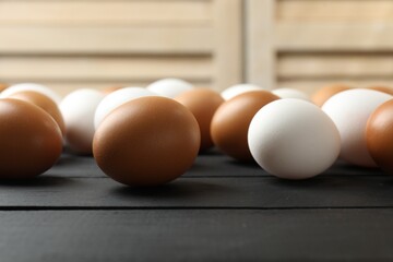 Many raw chicken eggs on black wooden table indoors, closeup
