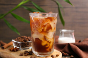Tasty iced coffee in glass, milk and beans on wooden table, closeup