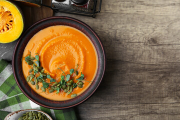 Delicious pumpkin soup with seeds and microgreens in bowl on wooden table, flat lay. Space for text