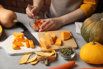 Woman removing pumpkin seeds at grey table, closeup