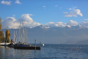 Peaceful autumn day at Lake Thun with sailboats, golden trees, and snow-covered Alps in the background.