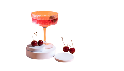 A fancy cocktail in a stemmed glass, cherries on a podium and scattered, against a black background