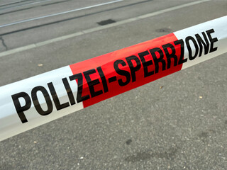 Red and white police line tape with POLIZEI-SPERRZONE text, closing off an area. A Swiss police barricade tape across a street, signaling a no-entry zone.