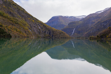 Fototapeta premium Autumn landscape in Skjolden, South Norway, with a calm lake reflecting the mountains and colorful foliage.