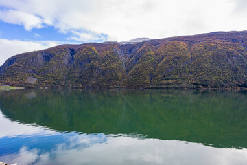 Obraz premium Autumn landscape in Lustrafjorden, South Norway, featuring clear water reflections, mountains, and colorful foliage.