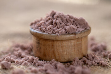 A small wooden bowl filled with purple powder, scattered around on a burlap surface