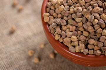 Closeup of dried chickpeas in a terracotta bowl on a textured burlap surface, showcasing their natural texture and color