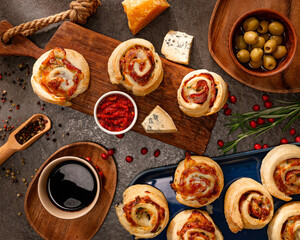 savory bakery rolls with sausage slices, blue cheese, hard cheese, olives, ground pepper, coffee, and spicy red dip on rustic wooden boards, festive homemade snack, cozy kitchen appetizer in daylight