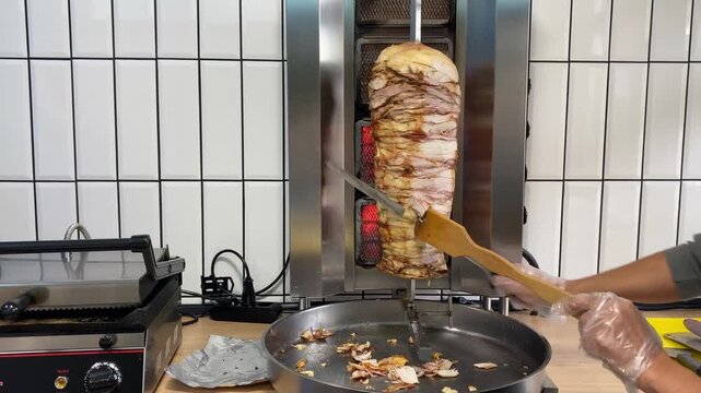 Meat is being sliced from a vertical shawarma grill using a knife. Cooking process in a kitchen or street food setting. Fresh, hot meat prepared for shawarma wraps.