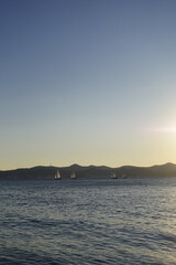 Sailboats sailing on the sea at sunset with mountains in the background
