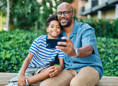 Portrait of father and son having fun using a mobile phone and taking a selfie photo with camera outdoors in park or nature,, family life, parenting, love and bonding concepts