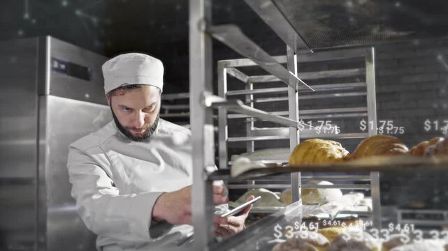 Camera view of handsome Caucasian male working at pastry factory. Holding tablet device with one hand while counting completed orders. Digital holographic prices floating above tasty bread.