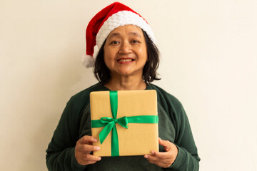 a woman wearing a green sweater, red Santa hat while smiling holding a gift with a green ribbon