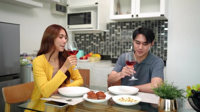 Asian adult couple enjoy romantic dinner at home kitchen dining area celebrating special occasion together drinking red wine