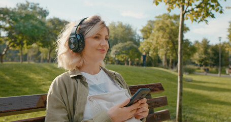 Mom listening to music for the unborn child while sitting on a bench in the park. Positive...