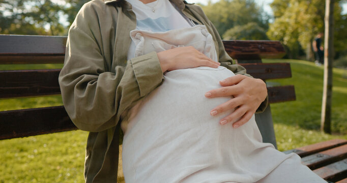 Mother leisure with positive attitude sitting outside. Pregnant belly touching and relaxing in the park and listening to music. Concept of Motherhood