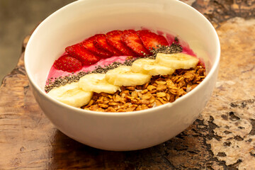 a sprinkling of nuts, a few slices of banana and a few pieces of strawberries served in one bowl on a wooden table