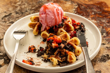 waffles, ice cream and strawberry slices served on a plate on a wooden table