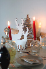 Table set for Christmas meal, with plates, wine, decorations and lit candles. Selective focus.