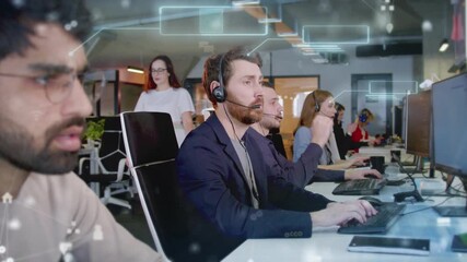 Male customer support agent wearing headset while working at computer with holographic chat windows above desk. Team of operators behind assisting clients in modern call center office. - Powered by Adobe