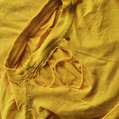 A worn yellow t-shirt with holes. Close up.