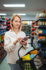 Woman using smartphone for grocery shopping in supermarket