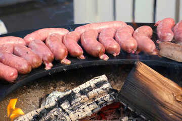 Uncooked sausages arranged on a circular grill above an open wood fire