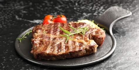 Delicious grilled beef steak with rosemary and tomatoes on dark textured table, closeup