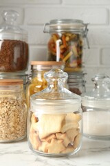 Glass jars with different products on white marble table, closeup
