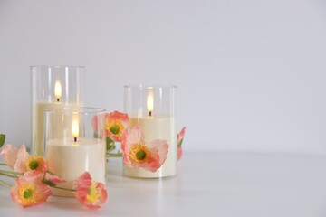 Decorative LED candles and beautiful flowers on white table indoors, closeup. Space for text