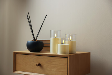 Decorative LED candles, reed diffuser and books on wooden bedside table near beige wall indoors