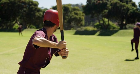 Baseball batter gripping wooden bat with helmet, watching baseball at park home plate with mound