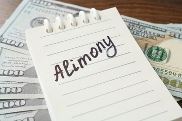 Obraz premium Notebook with word Alimony and money on wooden table, closeup