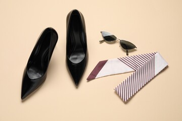 Pair of elegant black heels, sunglasses and scarf on beige background, flat lay. Stylish shoes