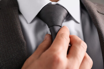 Man in suit adjusting his necktie on grey background, closeup