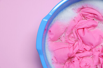 Plastic basin with clothes, water and foam on pink background, top view. Space for text