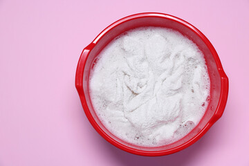 Plastic basin with clothes, water and foam on pink background, top view. Space for text