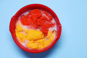 Plastic basin with clothes, water and foam on light blue background, top view