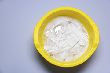 Plastic basin with clothes, water and foam on light grey background, top view. Space for text