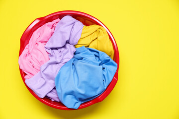 Plastic basin with clothes on yellow background, top view. Space for text