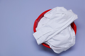 Plastic basin with clothes on light purple background, top view. Space for text