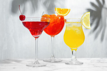 Glasses of tasty cocktails with garnish on white marble table