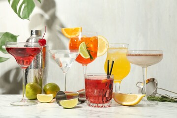 Glasses of tasty cocktails, ingredients, shaker, sieve and jigger on white marble table