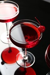 Glasses of tasty cocktails with garnish on mirror surface, closeup