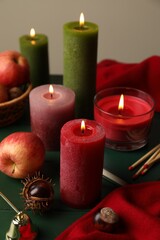 Composition with different burning candles on green table against grey background. Autumn atmosphere