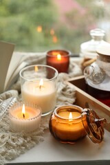 Burning candles, tea, book and plaid on windowsill on rainy day. Autumn atmosphere