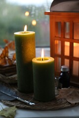 Burning candles, lantern, vintage books, ink and quill on windowsill on rainy day. Autumn atmosphere